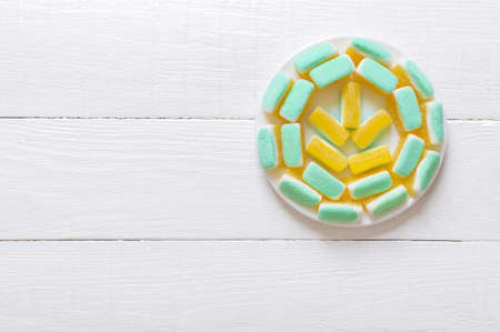 Sugar jelly candies in the form of melon slices on a plate on a white wooden background. Top view, free space.の写真素材