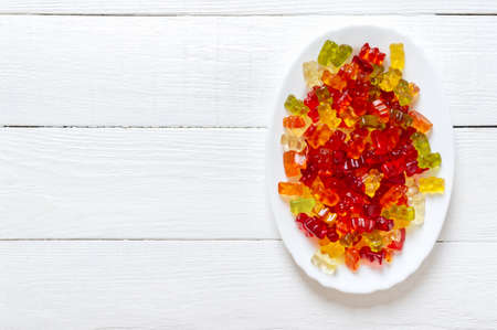 Gummy bears in a plate on a white wooden background. Bright jelly candies, vitamin supplements. Top view with copy space.の写真素材