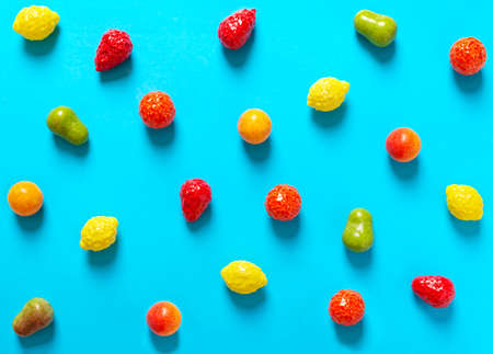 Bright chewy candies in the shape of fruits scattered on a blue background. Top view. Creative sweets background.の写真素材