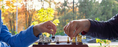 Two men play chess on a sunny autumn day in the park. Chessboard with figures close-up. Healthy lifestyle and pastime.の写真素材