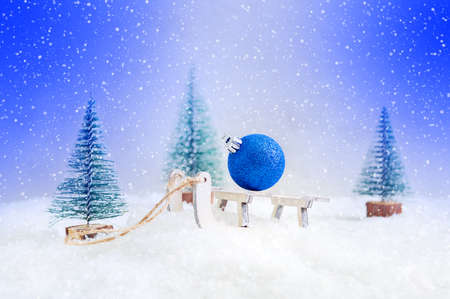 Beautiful festive Christmas, New Year card. Christmas ball on a toy sled in the snow among the firs.の写真素材
