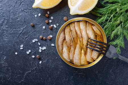 Open can with canned baltic smoked sprats in oil, one on fork, with lemon, dill. Top view, overhead,...