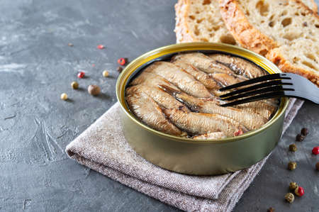 Sprats in an open tin can, stacked in rows, prick on a fork. Delicious canned fish.