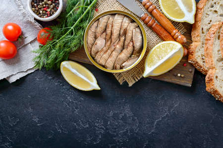 Smoked sardines in an open tin can, crispy whole grain bread, greens, lemon, fresh tomatoes. Top view, flat lay. Food background with copy space.の写真素材