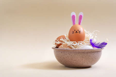 Easter eggs and Rabbit Egg with bunny ears and muzzle in a bowl of hay on pastel background with copy space. Easter composition.の写真素材