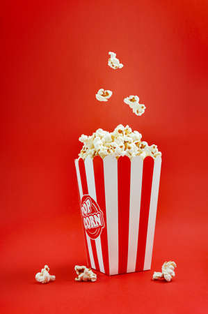 Falling popcorn in a striped cardboard box on a red background, vertical view. Popcorn levitation. cinema time.の写真素材