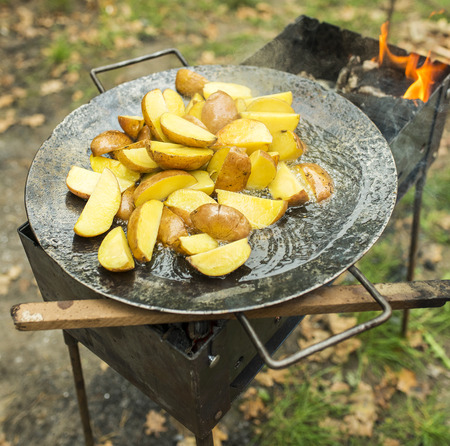 Fried potato in big melal pot. On grill and open fire, smoke.の写真素材