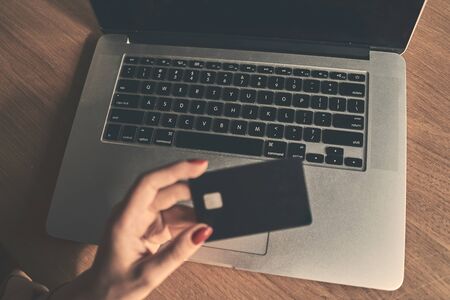Happy young girl holding plastic credit card while using laptop at the cafe.の写真素材