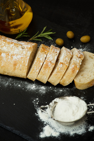 Ciabatta bread sliced, olives, olive oil and flour on a black stone surfaceの写真素材