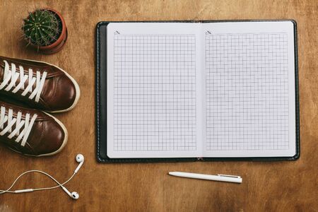 Girl diary or planning concept. Woman shoes, headphones, dairy and pen on a brown wooden desk. Copy...