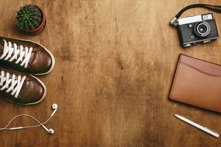 Woman girl lifestyle or travel background in brown colors. Earphones, shoes trainers, camera, notebook, pen, cactus plant on a brown wooden table. Copy space, place for text. Top view, flat lay.の写真素材