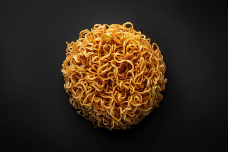 A circular cluster of cooked instant noodles, golden-brown in color, captured in close-up against a black background.の素材