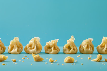 A row of steamed dumplings arranged on a blue background, with a few fallen dumplings scattered around them.の素材