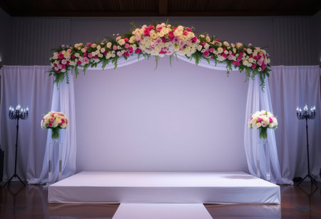 A wedding ceremony setup featuring a floral arch adorned with pink and white roses, greenery, and white drapes, with two bouquets on either side and candle stands.の素材