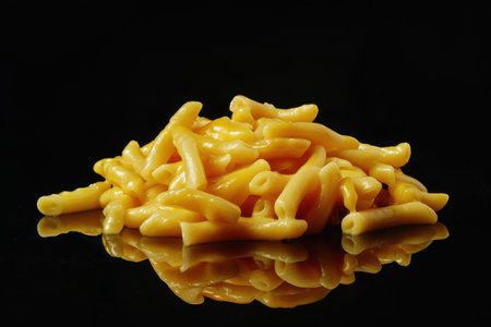 A close-up shot of macaroni and cheese, with reflections, against a black background.の素材