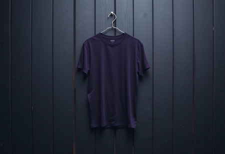A plain purple t-shirt hangs from a hanger against a dark wood backdrop.の素材