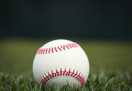 A close-up view of a baseball resting on green grass with a blurred background.の素材