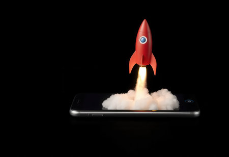 A red rocket ship taking off from a smartphone screen, symbolizing mobile app or website launch.の素材