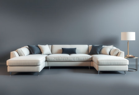 A white sectional sofa with black pillows and a lamp on a side table, in a minimalist living room setting.の素材