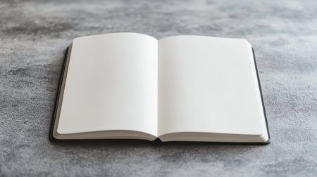 An open, blank notebook with white pages lies on a textured gray surface.の素材