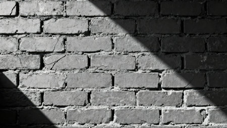 Monochrome  of damaged gray masonry wall texture featuring thick mortar and surface cracks, dramatically split by a bright diagonal shaft of natural or artificial light.の素材