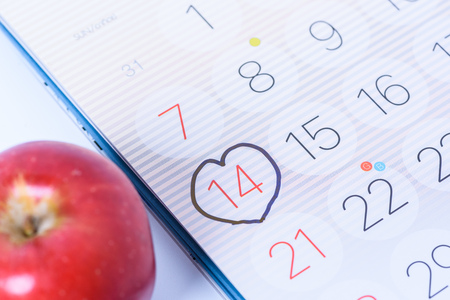Calendar page with a black hand written heart highlight and red apple on date of February 14 Valentine's dayの写真素材