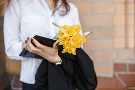 Young woman relaxing with yellow flowers. The girl picks up the flowers. The lady writes in her notebook. A woman stands by the brick wall.の写真素材