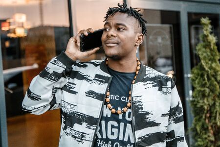 Young black businessman talking on mobile phone and working. Happy bearded African businessman using phone. Concept of young people working mobile devices. Blurred background.の写真素材