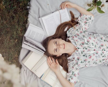 Girl lying in grass, reading a book. Girl with books. Notebooks and diaries.