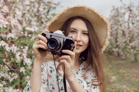 Nature Photographer taking pictures outdoors. Beautiful girl in a hat and dress in an apple orchard....