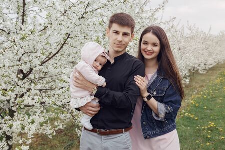 Family couple with their young children in the park. Husband and wife with children in the garden near the flowering trees.の写真素材