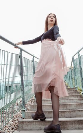 Beautiful girl in a black blouse and pink skirt climbs the stairs up. Young pretty woman walking up the stairs in the city. BUW. Warsaw.の写真素材
