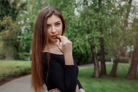 Stylish girl paints her lips with lipstick on a walk. Cute young girl applies makeup in the park. Poland.の写真素材