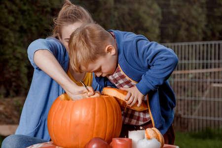 A boy and his mother cut a pumpkin. A young mother and son are preparing a pumpkin for Halloween. Peel an orange pumpkin.の写真素材