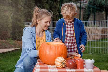 A boy and his mother cut a pumpkin. A young mother and son are preparing a pumpkin for Halloween. Peel an orange pumpkin.の写真素材