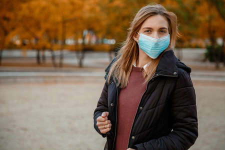 Girl with a phone in a mask. Woman in medical mask outdoors in autumn. Selfie in a mask.の写真素材