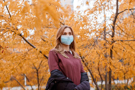 Girl in a mask near the business center. Woman in medical mask outdoors in autumn. Epidemic in the fall. Female student during the epidemic.の写真素材