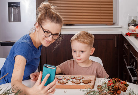 enjoying winter time at home and making cookies. Mom and her son shape the dough for baking homemade holiday gingerbread on background with garlands.の写真素材
