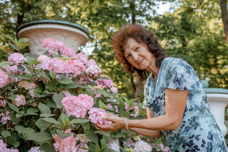 Woman in park .. Senior Working In Garden. Close-up portrait of an older woman on walk with flowers....