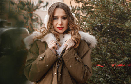 Beautiful young woman sits on the stairs near fir tree and christmas gifts at winter holidays. A pretty girl spends time at the Christmas market in the festive.の写真素材