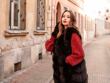 Elegant girl walk in a winter city. Beautiful lady with blond hair. Portrait of beautiful blond woman dressed in warm clothes. A woman wears green puffer jacket with hood, white pants, and boots.の写真素材