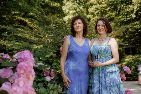 Happy woman have fun in evening gown. Mom and her daughter laughing and walking at the park. Two middle aged women chatting and looking at each other dressed in long dresses. Mother and daughter.の写真素材