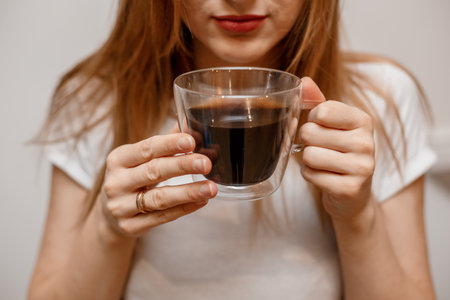 Woman hands holding mug of hot drink. She is smiling and holding a cup of coffee in hand split up in order to inhale the aroma of coffee. Young beautiful happy woman with cappuccino.の写真素材