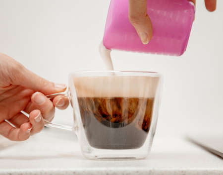 Barista pouring steamed milk into coffee cup. A milk jug and a cup of coffee, makes cappuccino, pouring whipped milk into espresso.の写真素材