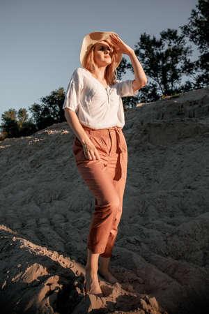 Young beautiful lonely woman with long hair in with straw hat. A lonely girl goes down the sand dunes. Summer fashion portrait outdoor.の写真素材