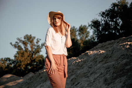 Young beautiful lonely woman with long hair in with straw hat. A lonely girl goes down the sand dunes. Summer fashion portrait outdoor.の写真素材