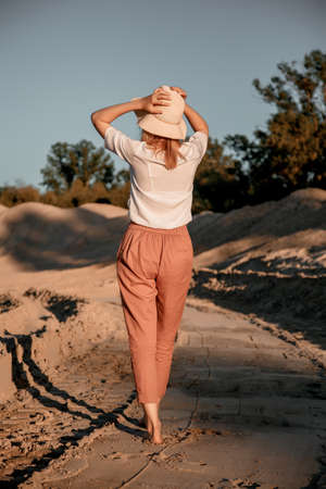 Young beautiful lonely woman with long hair in with straw hat. A lonely girl goes down the sand dunes. Summer fashion portrait outdoor.の写真素材