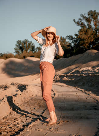 Young beautiful lonely woman with long hair in with straw hat. A lonely girl goes down the sand dunes. Summer fashion portrait outdoor.の写真素材