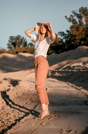 Young beautiful lonely woman with long hair in with straw hat. A lonely girl goes down the sand dunes. Summer fashion portrait outdoor.の写真素材