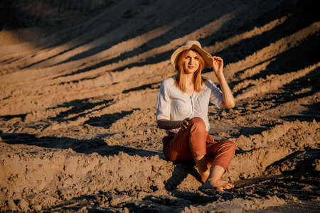 Young beautiful lonely woman with long hair in with straw hat. A lonely girl goes down the sand dunes. Summer fashion portrait outdoor.の写真素材